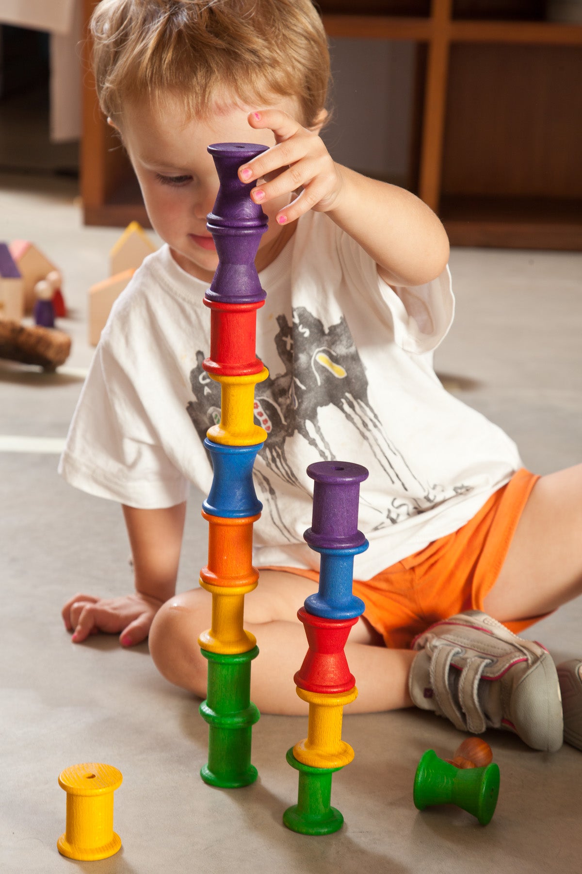 a small child plays with rainbow coloured wooden spools. They are stacking the spools in two towers,