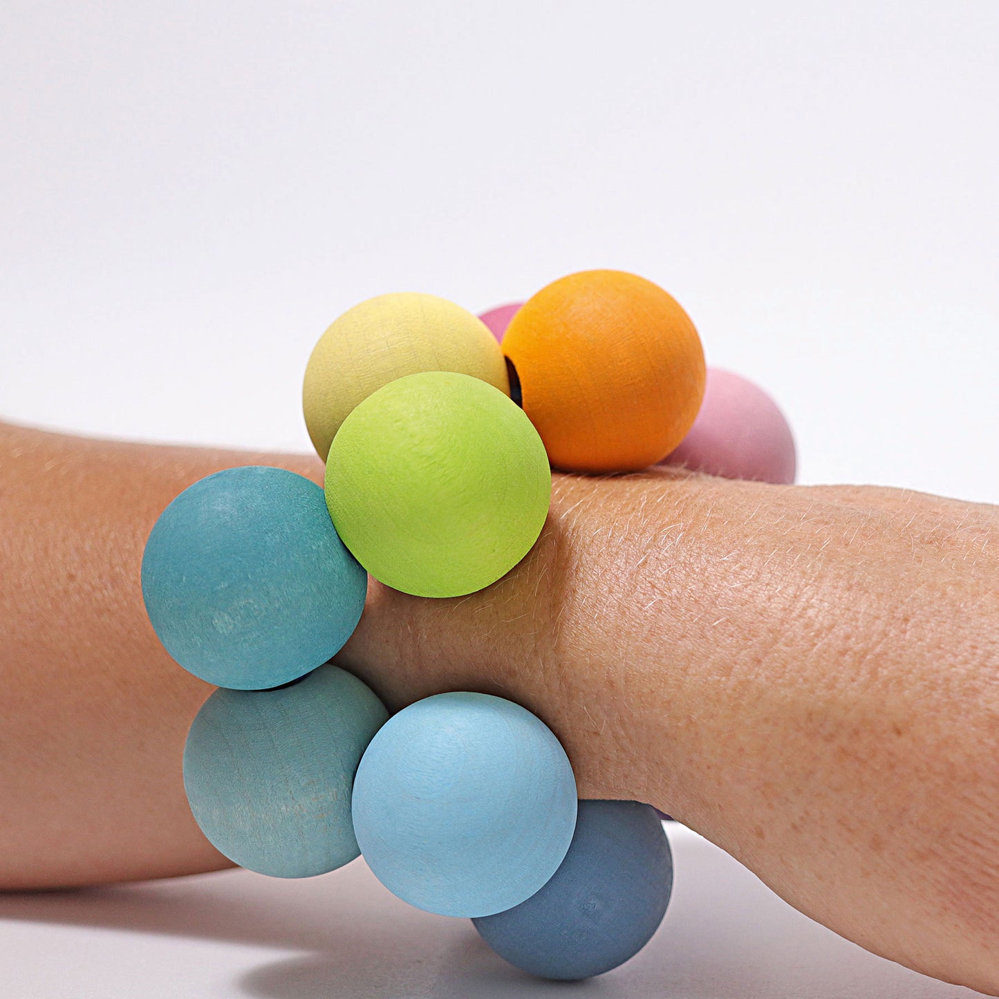 a wooden baby grasper in pastel rainbow colours is worn on a wrist as a bracelet