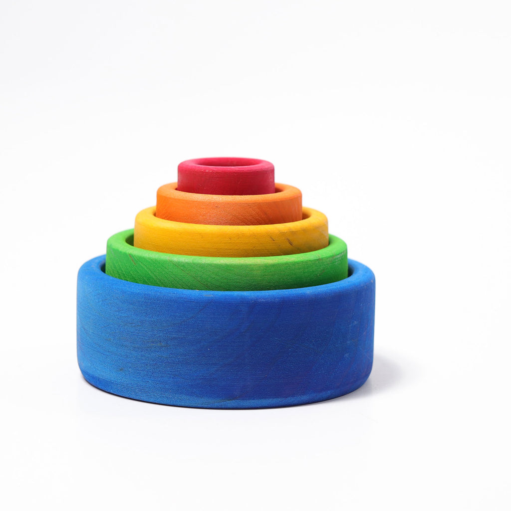 Wooden stacking bowls are nested inside each other.  They are in bright rainbow colours